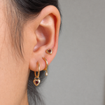 Fearless Heart solid-gold stacked earrings worn on the ear, clean neutral background